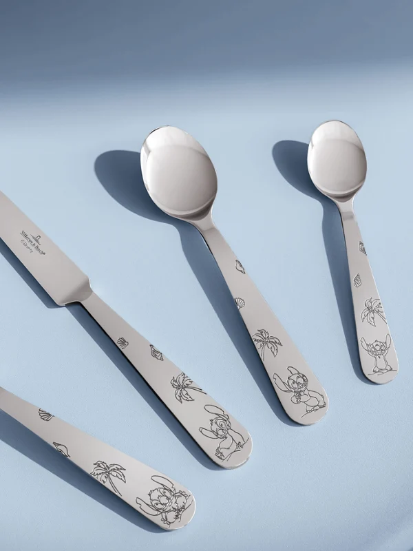 Cuatro piezas de cubertería infantil de la colección Disney Stitch sobre un fondo azul claro. Cuatro piezas de cubertería infantil (tenedor, cuchillo, cuchara y cucharilla) de la colección Disney Stitch dispuestas sobre un fondo azul claro.