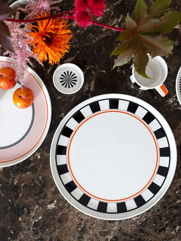 Service de table Memphis de Villeroy & Boch avec des assiettes décoratives, une tasse, des tasses et des prunes sur une surface en marbre brun décorée de fleurs brillantes.
