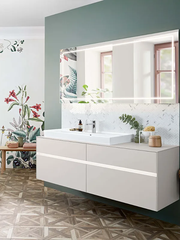 A Collaro washbasin, furniture and bath in a bathroom with floral wallpaper.