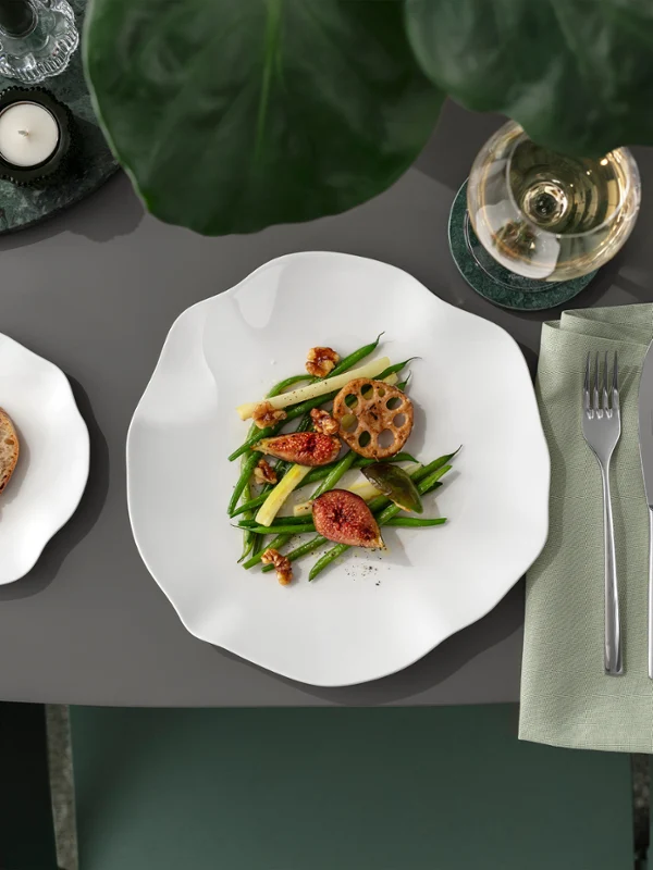 A Pura plate with salad, bread and wine on a laid table, seen from above.