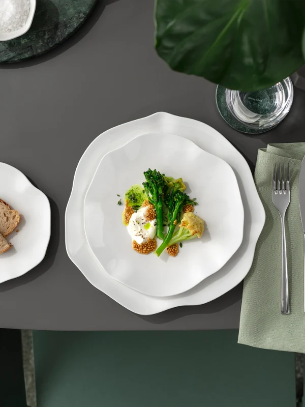 Ein Pura Teller mit Gemüse und ein Beilagentelle auf einem grauen Tisch Ein Pura Teller mit Gemüse und Ei, ein Beilagenteller mit Brot und Besteck auf einer Serviette auf einem grauen Tisch.