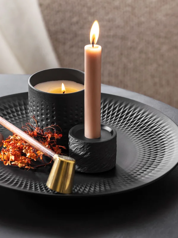 Una candela accesa con incenso e fiori secchi su un piatto decorativo nero Manufacture.