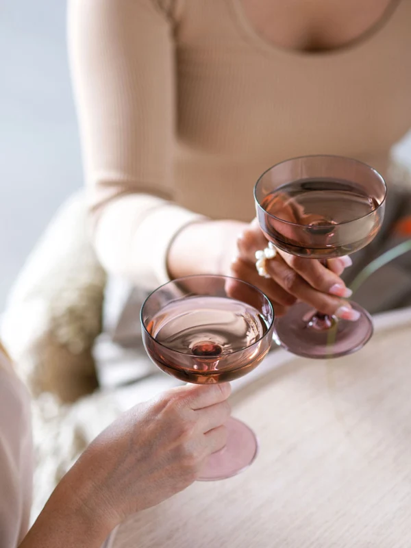 Twee mensen met Like Glass glazen gevuld met drankjes van Villeroy & Boch en zittend aan een tafel gedecoreerd met een rood bloemstuk en een boek met de inscriptie “Mallorca”.	