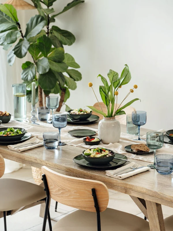 A wooden dining table for four with crockery and a plant centerpiece.