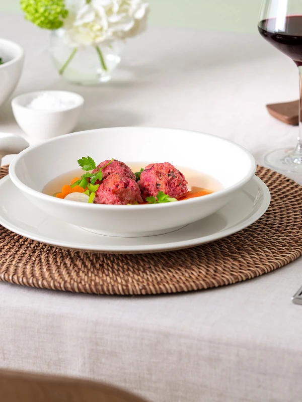 A table setting with a Artesano bowl of soup, bread, salad, a glass of wine, and utensils on a woven placemat.