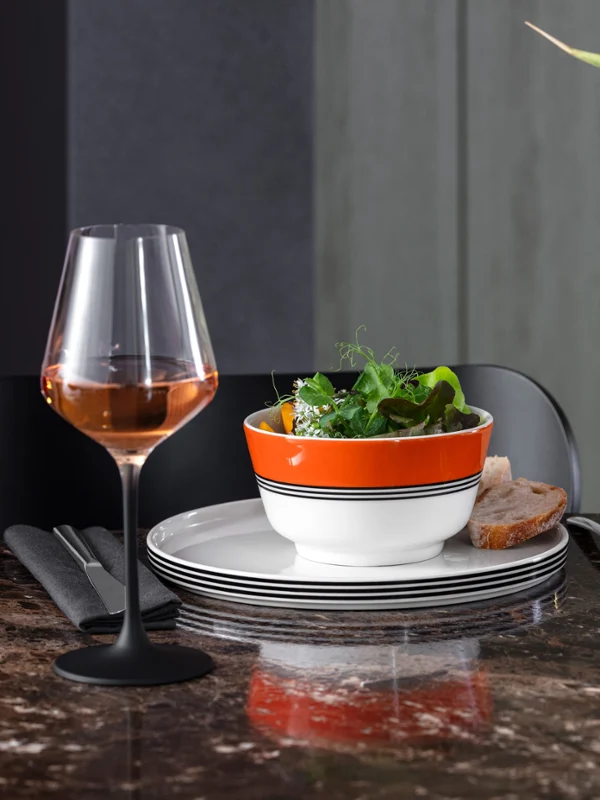 Memphis by Villeroy & Boch ideal for starters A dining room with a Memphis salad bowl, a wine glass, striped Memphis plates, a tropical flower in a Memphis vase and a marble table top.