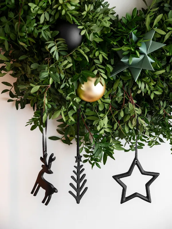 Green door wreath decorated with hanging Black XMAS ornaments in front of a white wall.