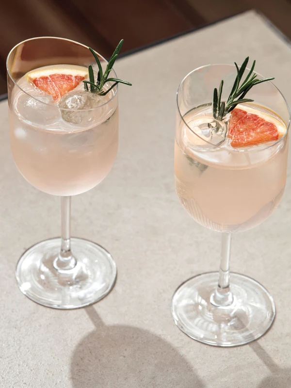 Twee NewMoon rode wijnglazen met rozemarijn-grapefruit cocktails op een houten tafel.