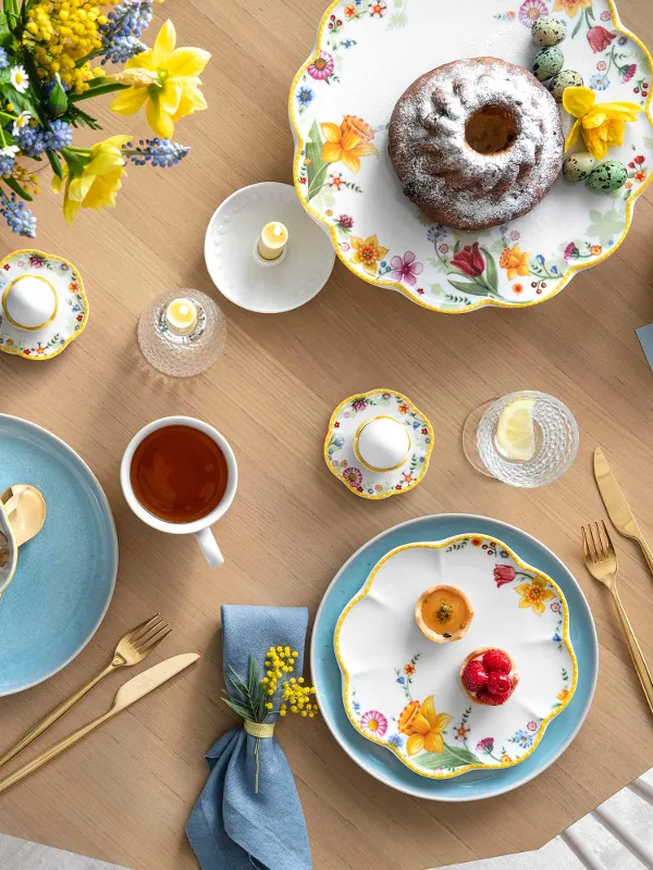 A springtime table setting with Spring Awakening and Crafted dinnerware, a Bundt cake, a serving bowl of oatmeal with berries, a cup of tea and decorative eggs.