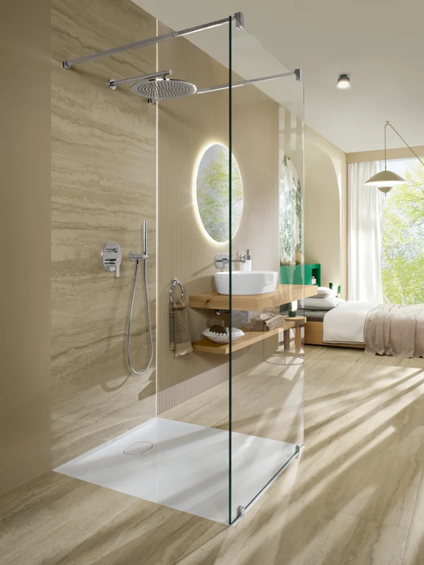 Villeroy & Boch Ecora shower tray in an open walk-in shower with travertine-look surfaces, beside a bright bedroom with a garden view.