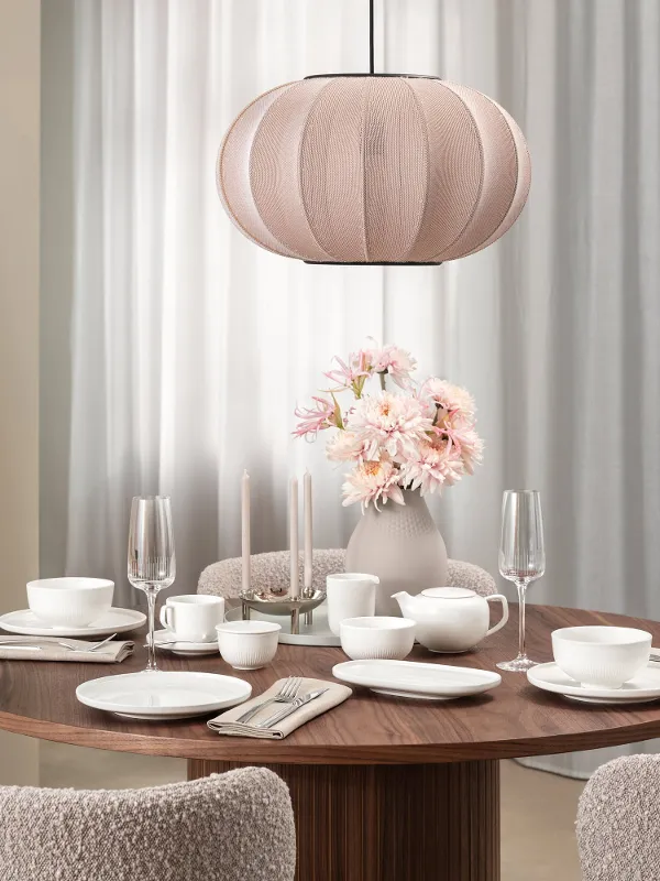 Une salle à manger moderne avec une table ronde en bois, de la vaisselle Afina blanche, des verres Afina, des fleurs roses et une suspension beige.