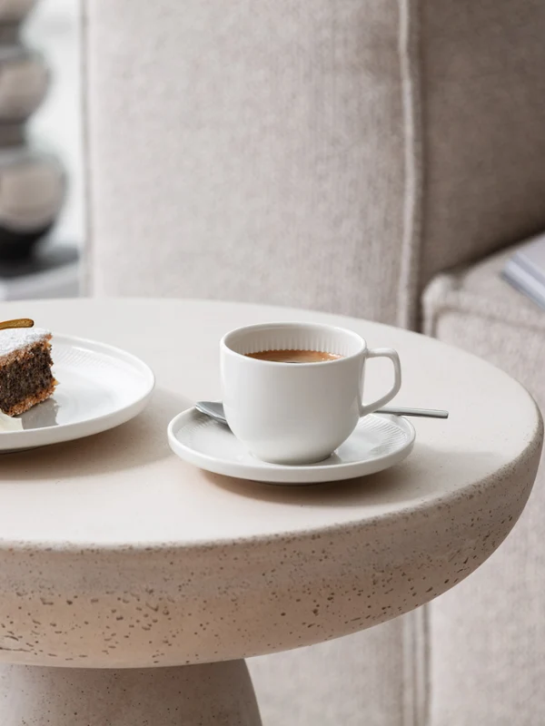 A cup of coffee and a plate of cakes served on a modern side table with Afina crockery from Villeroy & Boch.