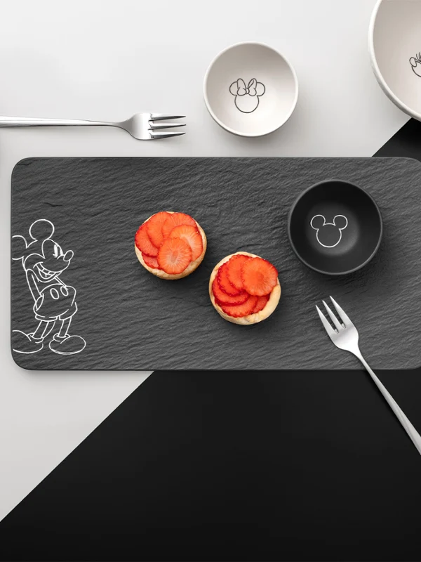 Vista superior de una esterilla rectangular, platos, cuencos y tenedores. Vista superior de una mesa puesta de la colección Manufacture Mickey con tartaletas de fresa sobre un mantel rectangular, platos, cuencos y tenedores.