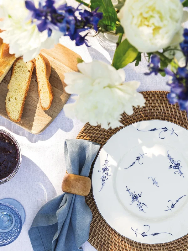 On a laid table there is a Villeroy & Boch Old Luxembourg plate, a cloth napkin, a knife, a fork and a jar of dark jam.