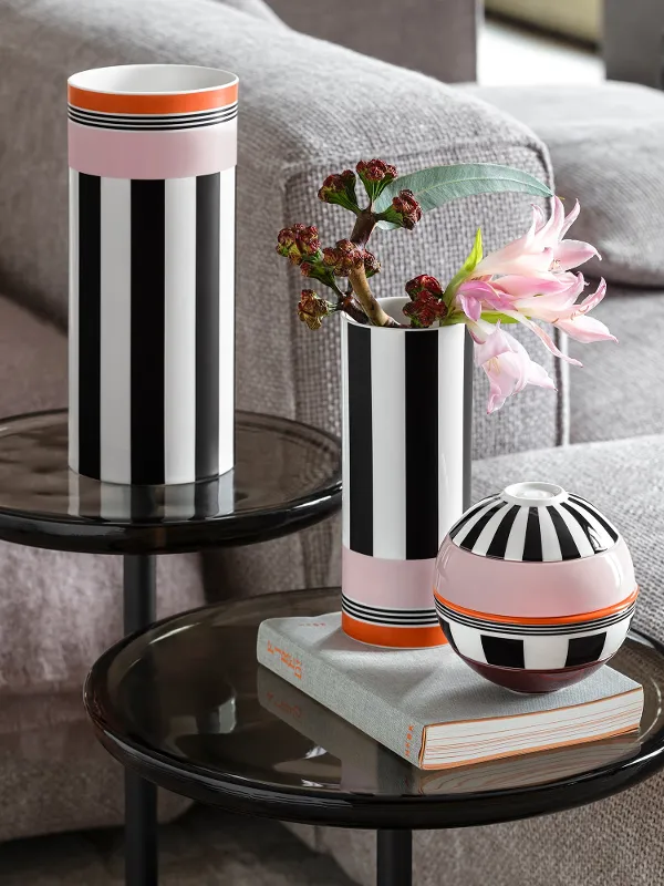 Deux vases à rayures noires et blanches et un récipient rond sont posés sur des tables en verre à côté d'un canapé gris, l'un des vases contient des fleurs