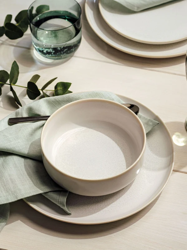 Eine weiße Crafted Bol auf einem Crafted Teller gedeckt mit mint grünen Servietten und Eukalyptus.