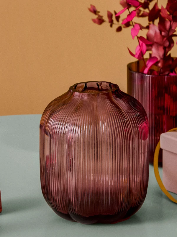 Fleur ribbed glass vases and colorful candles Close-up of ribbed glass vases in berry shades, featuring colorful taper candles in matching glass holders and a pink pillar candle on a gift box.