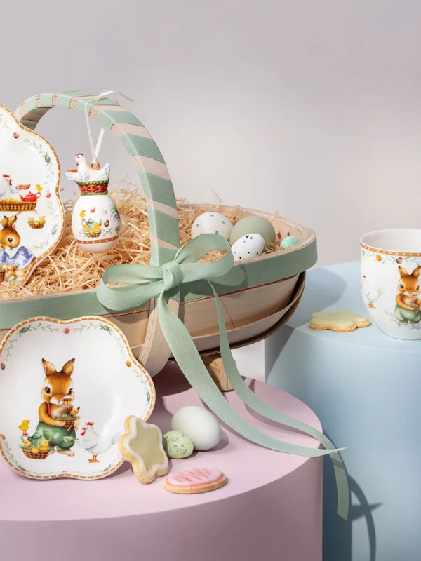 Annual Easter Edition 2026 tableware with bunny designs, eggs, a mug, and cookies arranged on pastel-colored platforms.