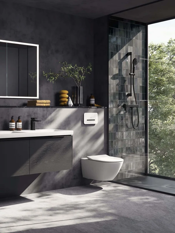 Łazienka ze skośnym sufitem cała w czerni Nowoczesna łazienka z ciemnymi płytkami ściennymi, podświetlanym kwadratowym lustrem More to See Lite, czarną umywalką stojącą na blacie Loop & Friends na wiszącej szafce podumywalkowej Antao i uchwytem na ręczniki z różowym ręcznikiem, wszystko w delikatnym świetle dziennym.