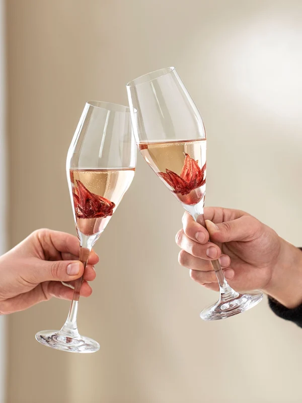 Dwie osoby wznoszą toast kieliszkami La Divina Na neutralnym tle dwie osoby wznoszą toast kieliszkami La Divina marki Villeroy & Boch, w każdym z nich jest kwiat hibiskusa.