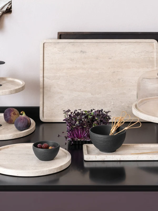 Keukenwerkblad met elegante Manufacture Travertin-schalen, waarop vijgen, brie, brood en een kom groenten worden gepresenteerd.