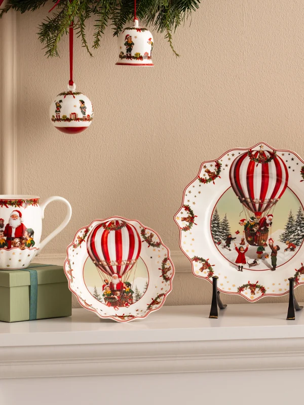 Festive ceramic plates, cups, and bowls with motifs of red hot air balloons from Villeroy & Boch are presented together with red flowers and Christmas decorations.