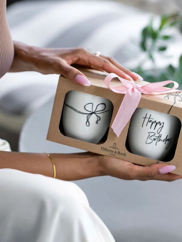 Person holding a gift box with a pink bow containing two 'Happy Birthday' Statement mugs.