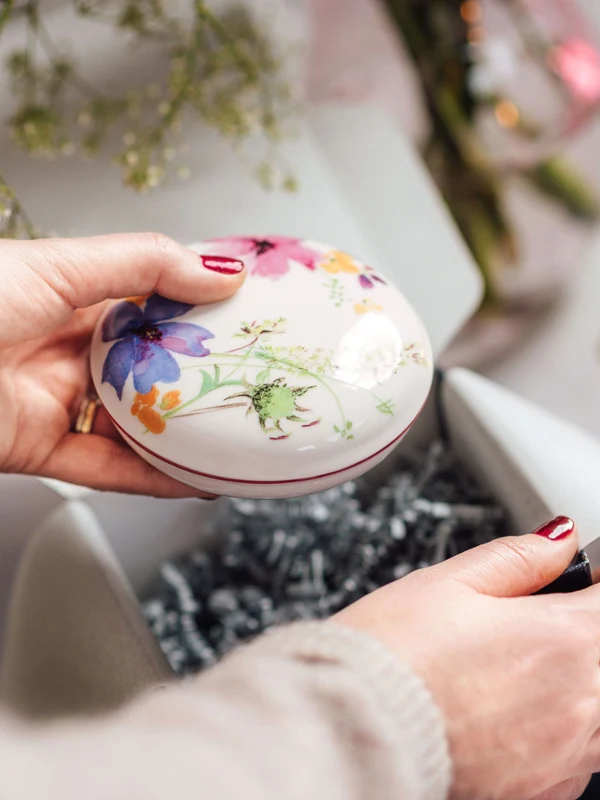 Ręce trzymają misę Mariefleur od Villeroy & Boch z kwiatowym wzorem. Ręce trzymają misę Mariefleur od Villeroy & Boch z kwiatowym wzorem, rozpakowywaną obok zapalonej różowej świecy.