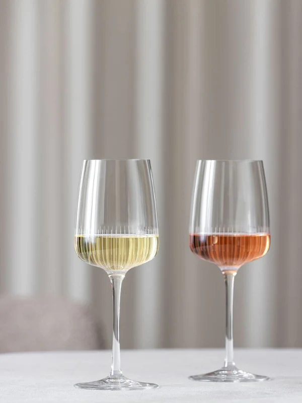 Twee Afina wijnglazen van Villeroy & Boch, één gevuld met witte wijn en de andere met rosé, staan op een tafel naast een vaas met roze bloemen.