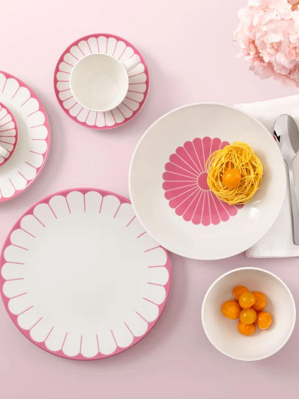 Table setting with Villeroy & Boch Fleur Cassis plates, pasta, clementines, and flowers on a pink background.