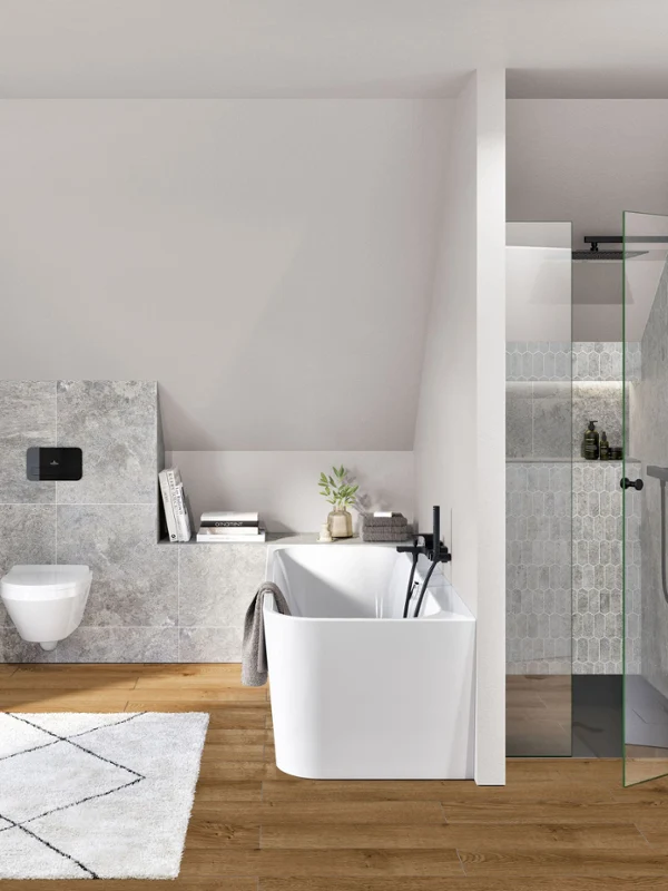 Biała wanna z czarną baterią obok białej toalety i przeszklonego prysznica Nowoczesna łazienka z wiszącą miską WC Architectura, wanną wolnostojącą, przeszklonym prysznicem, dywanem i drewnianą podłogą. W strefie prysznica znajdują się wbudowane półki z przyborami toaletowymi.