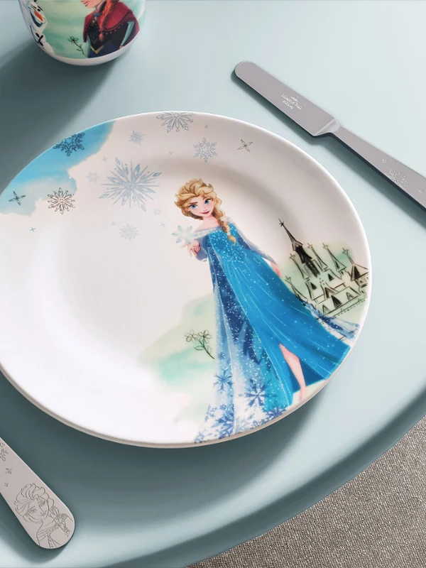 Platos y cubiertos de la colección Disney Frozen sobre una mesa azul claro. Un plato con motivos de Frozen, tenedor y cuchillo a ambos lados, también de la colección Disney Frozen, sobre una mesa azul claro.