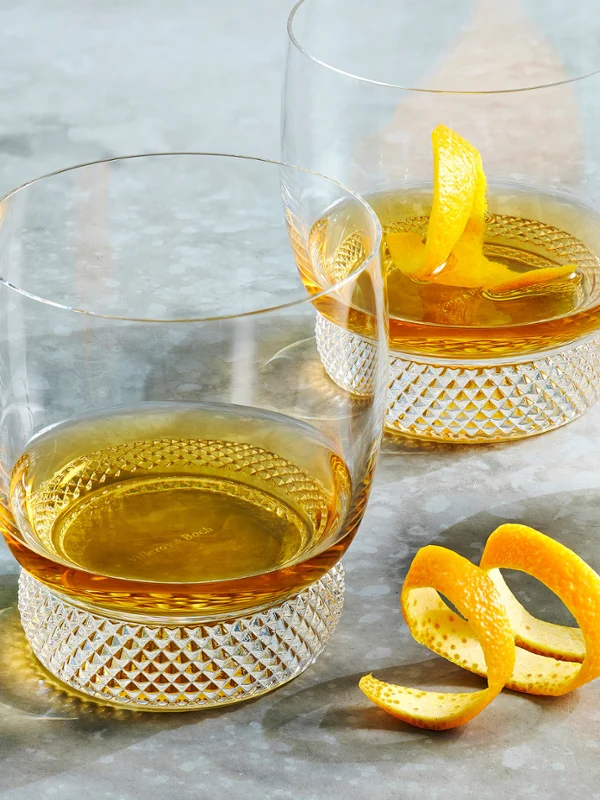 The Octavie Tumblers Gift Set, featuring two elegant crystal glasses filled with whisky, is complemented with a Manufacture Rock bowl filled with green olives.