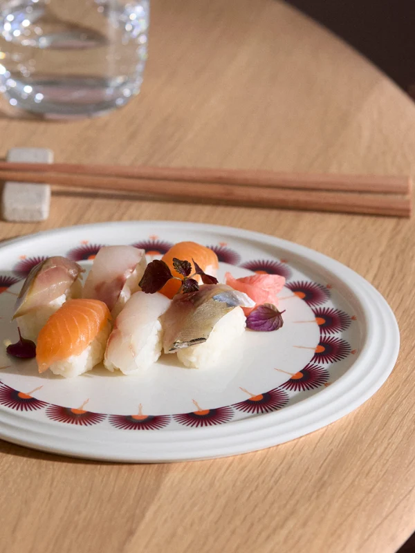 La Boule Kyoto sushi On a wooden table sits a plate from La Boule Kyoto with various types of sushi, alongside chopsticks, a glass of water, and a wine glass.