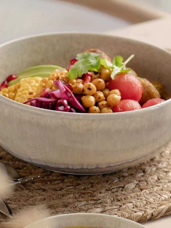 A Perlemor ceramic bowl with various vegetables A Perlemor ceramic bowl containing various vegetables, chickpeas and greens stands on a woven placemat, next to which are chopsticks.