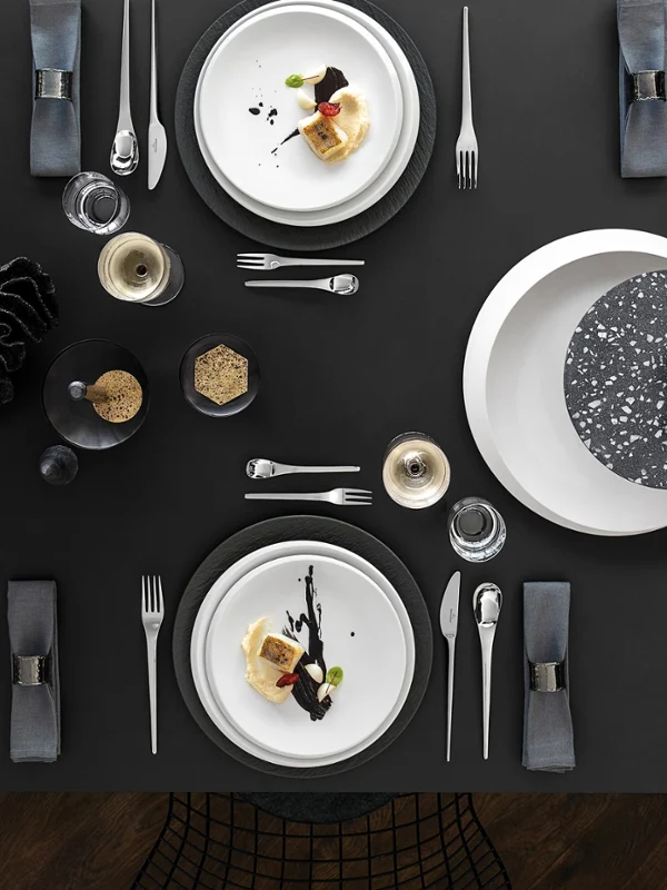 Ein moderner schwarzer Esstisch für sechs Personen mit Vorspeisentellern, Besteck, Gläsern und dekorativen Tafelaufsätzen.