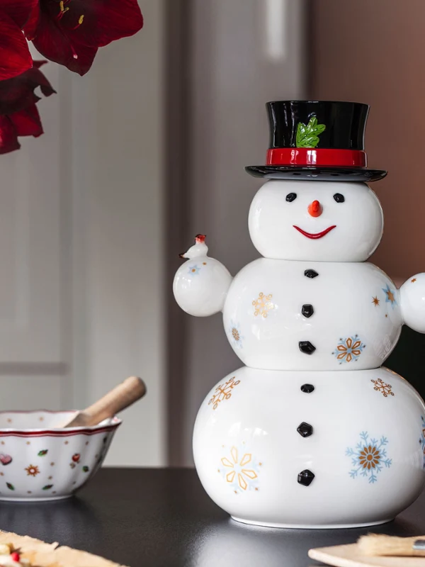 Christmas Toys Memory snowman with a Toy's Delight bowl A Villeroy & Boch Father Christmas with a black hat and red bow on a table next to a sugar bowl, a mixing bowl and red flowers. Blurred Christmas lights can be seen in the background.