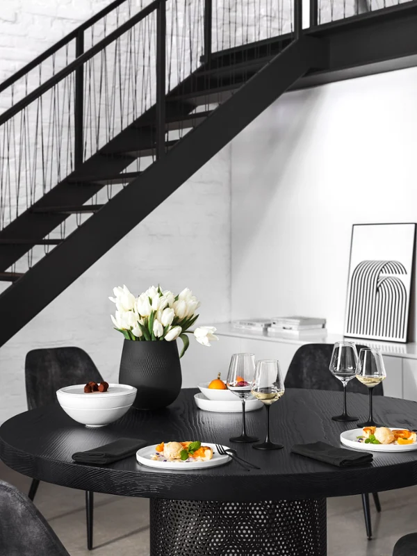 White La Boule modernly arranged A modern dining area with a black round table for three people, elegant white dinnerware, and minimalist decor and wall art.