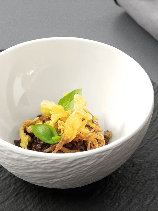 Manufacture bowl on top of a plate Manufacture white bowl on a black plate, with food in the bowl.