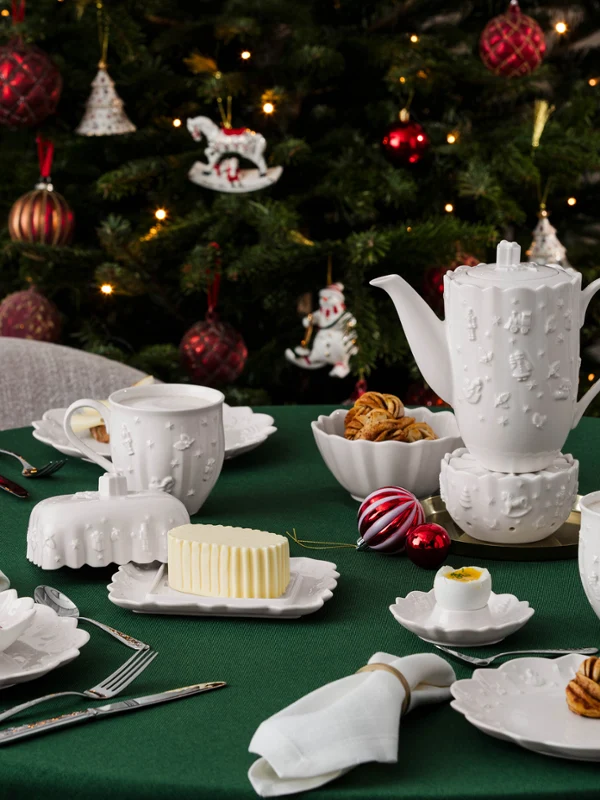 Toy's Delight Royal Classic coffee pot A set table with white porcelain tableware from Villeroy & Boch, pastries, and butter in a butter dish in front of a decorated Christmas tree.