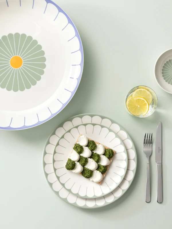 Une table dressée avec des assiettes et des bols décoratifs, une tranche de pain avec des légumes sur une assiette, à côté une fourchette et un couteau et à droite des fleurs blanches. Une table dressée avec des assiettes et des bols décoratifs, une tranche de pain avec des légumes sur une assiette, à côté une fourchette et un couteau et à droite des fleurs blanches.