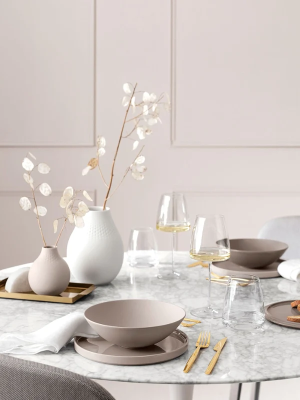 La Boule Pure Beige on a dining table along with MetroChic glasses A dining table with a white table cloth and a vase of flowers, set with La Boule Pure Beige and MetroChic wine glasses.