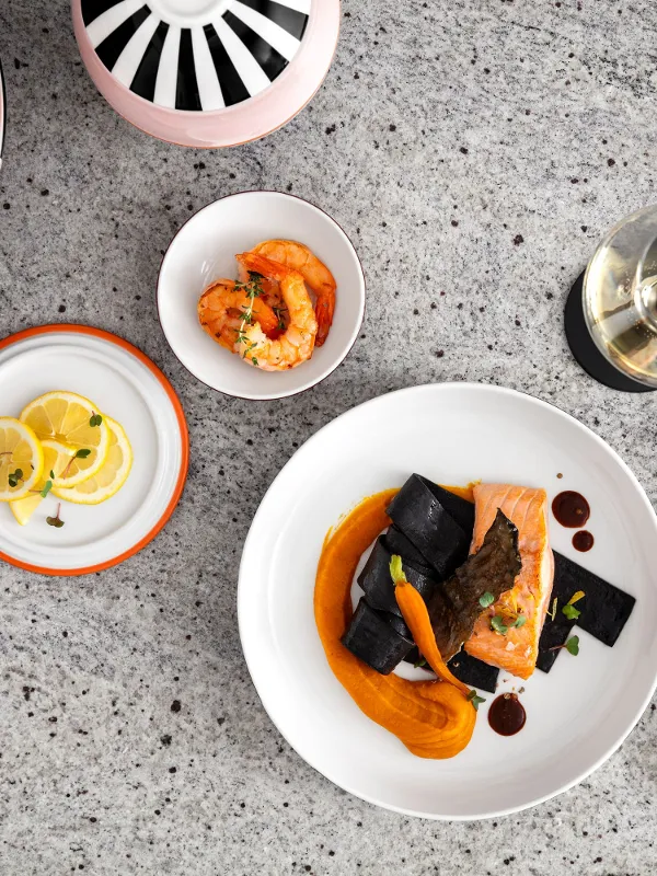 Stoviglie in ceramica Memphis dal design moderno, servite con salmone, gamberi e fette di limone su un tavolo di pietra.