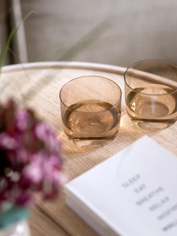 Two orange Like glasses on a wooden table next to a bouquet of flowers and a book.