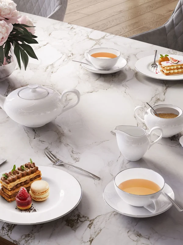 Elegantes Anmut Teegedeck auf einem Marmortisch, bestehend aus einer Teekanne, Tassen und Milchkännchen mit Tee mit Gebäck.
