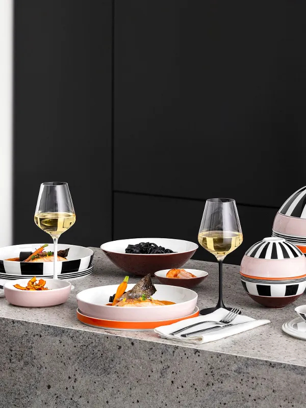Un tavolo moderno con La Boule e La petite Boule a fantasia, bicchieri da vino e snack su un piano di lavoro grigio in una cucina minimalista.