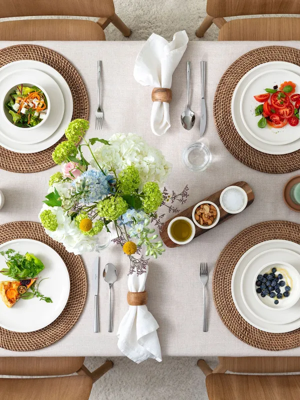 Top view of a rustic table setting for four people with food served on Villeroy & Boch Artesano Original porcelain: dinner and breakfast plates, bowls, pasta dishes, dip bowls, round serving bowl, antipasti plate, salad servers, and the Piemont cutlery. A warm and inviting scene perfect for casual meals with family or friends.