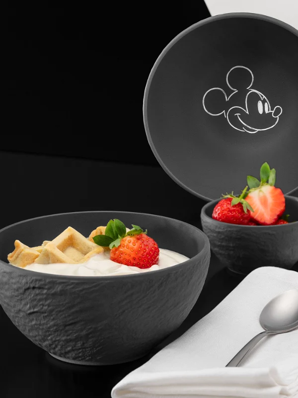 Copa negra con yogur y fresas Un cuenco negro de Manufacture Rock Mickey con yogur, fresas y galletas saladas, junto a él un cuenco a juego, una cuchara y una servilleta doblada.