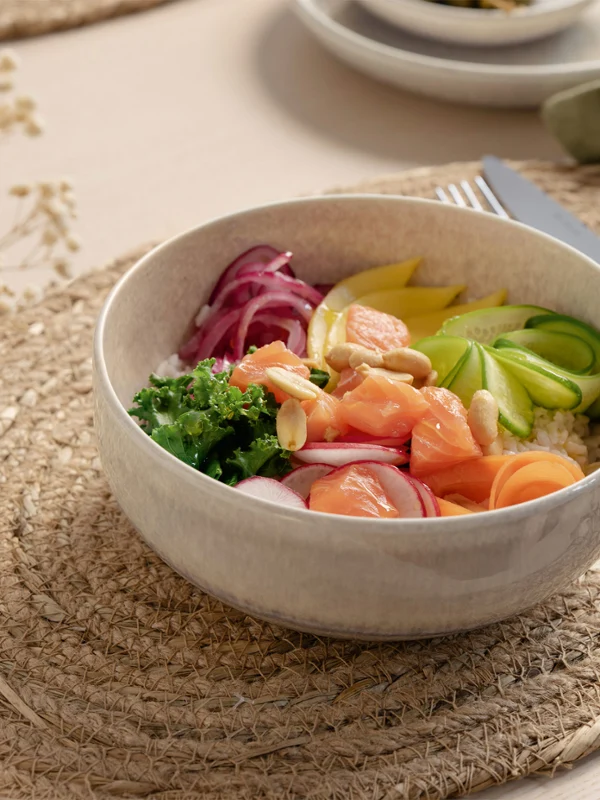 A Perlemor bowl on a woven placemat A Perlemor bowl of rice with slices of salmon, avocado, pickled onions, cucumber and parsley on a woven placemat.