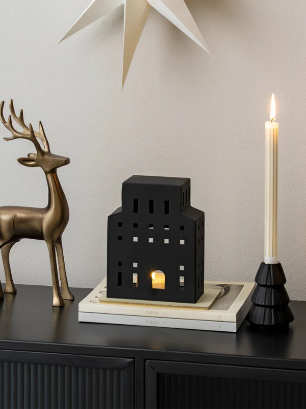 Dos renos de metal, unos candelabros y una linterna negra con forma de casa sobre un aparador negro.